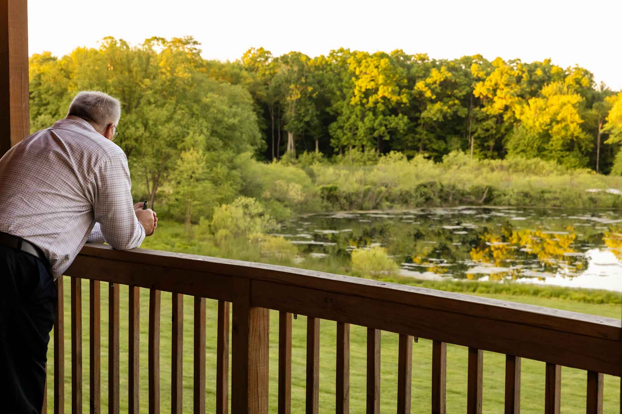 wedding guest leans over the barn railing overlooking the lake at sunset at the outdoor wedding venue in butler, pinehall at eisler farms